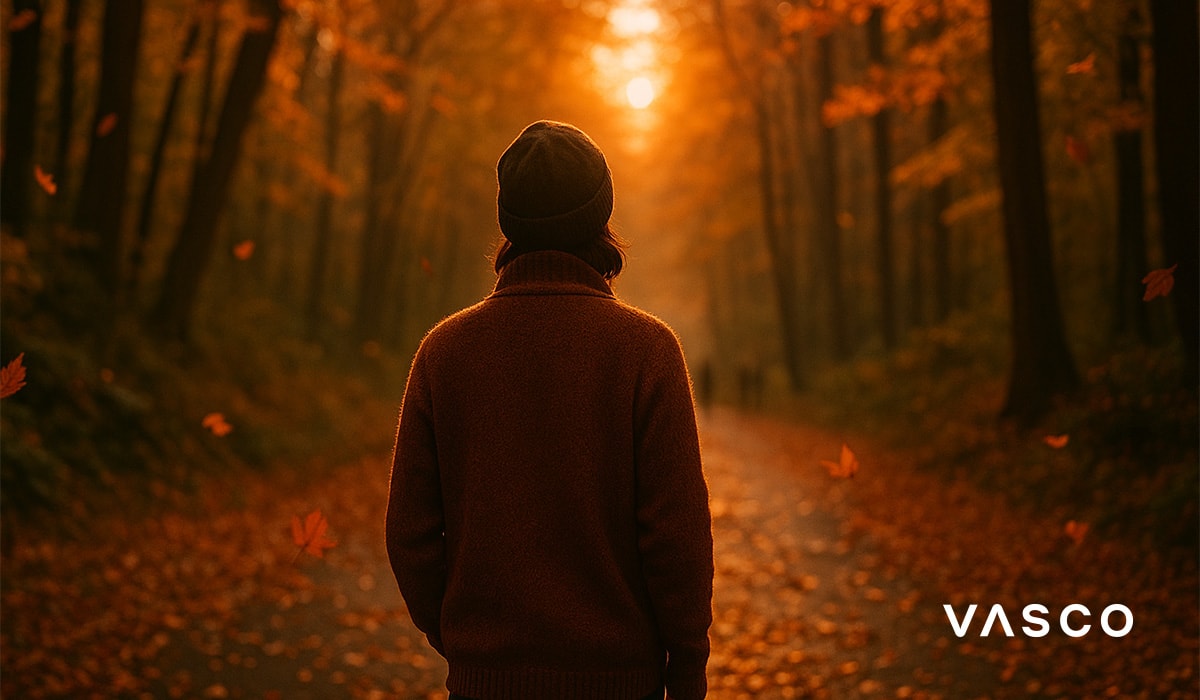 Persona con maglione marrone che cammina attraverso la foresta con le foglie che cadono.