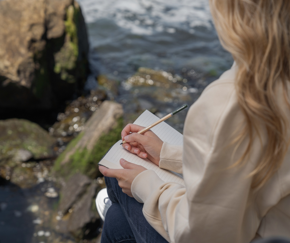 a woman writes in a notebook by the sea