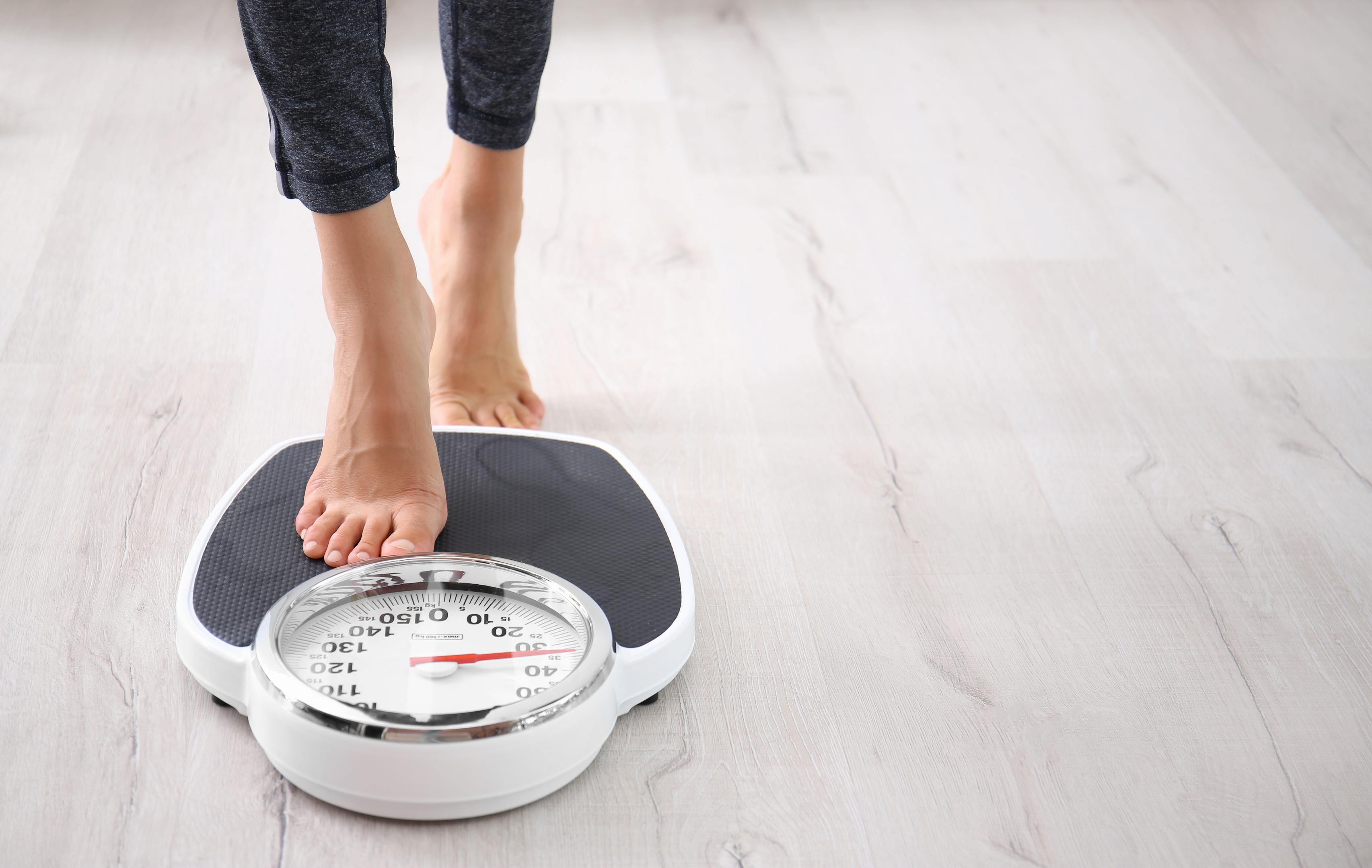 Person stepping onto a bathroom scale, representing weight loss before tummy tuck surgery.