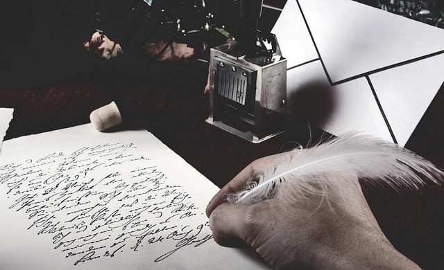A person writing poetry with a feather pen, surrounded by desk items, such as an envelope.