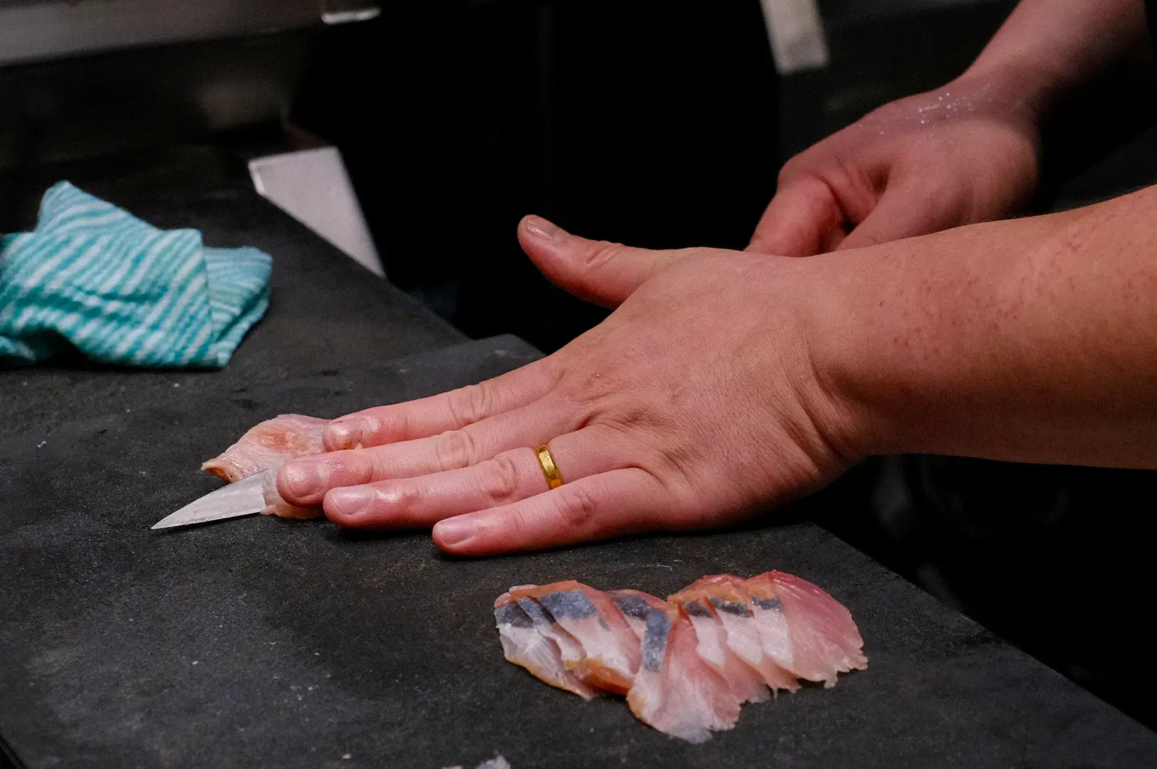 Professional sushi chef precision slicing raw fish fillet on a black cutting board to prepare fresh sashimi.