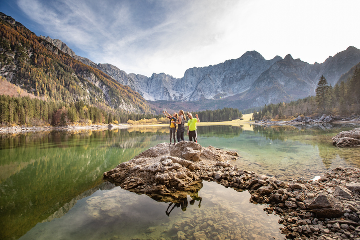 Three friends standing on a jetty taking photos of the mountains surrounding them.