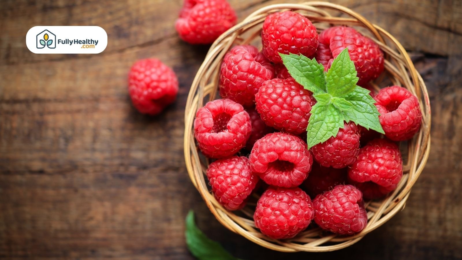 Basket of fresh raspberries on wooden table with green mint leaves