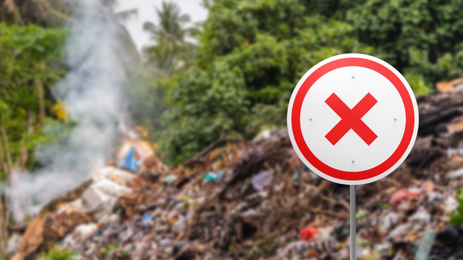 Tanda larangan di depan area pembuangan sampah terbuka yang masih mengeluarkan asap.