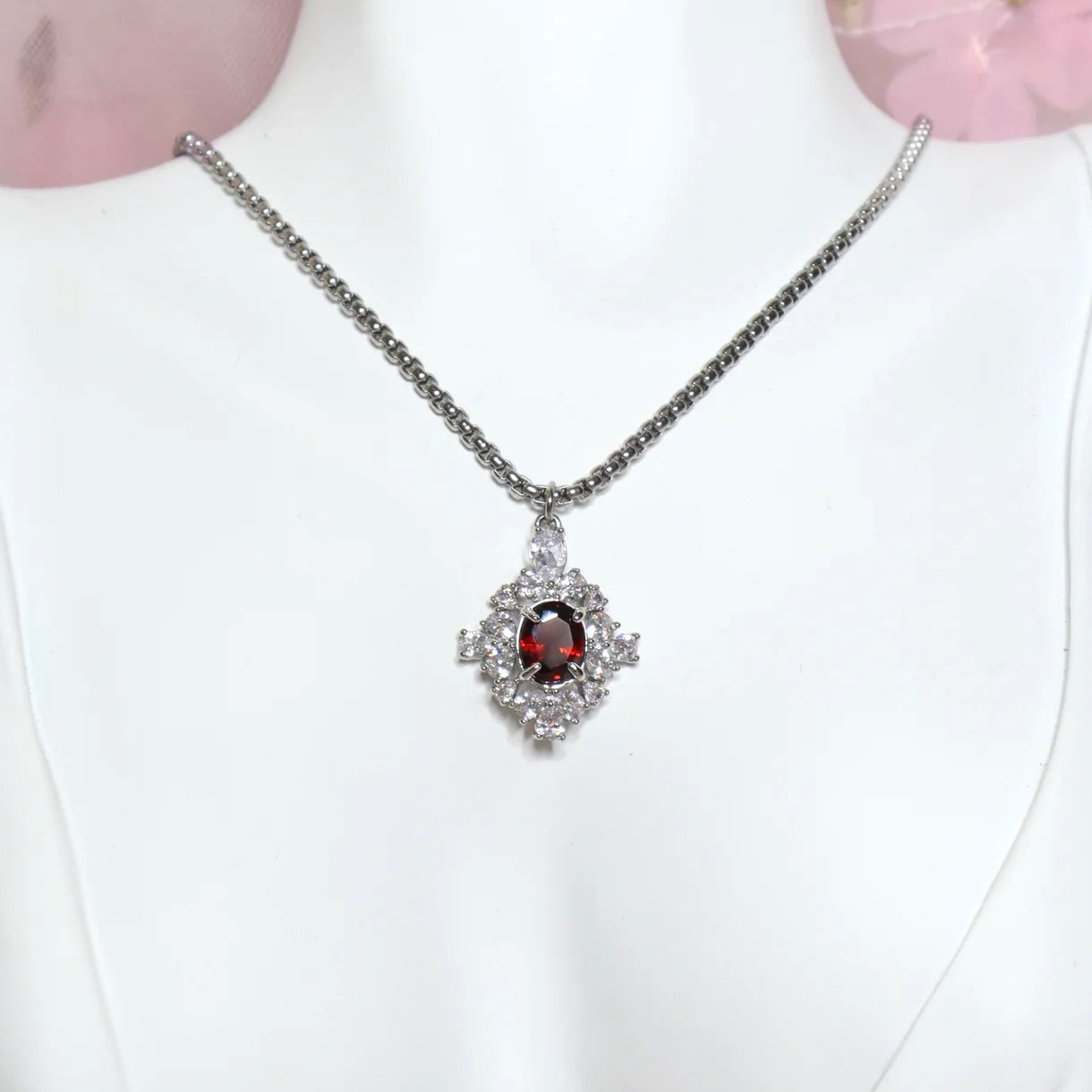 Close-up of a white mannequin wearing an elegant vintage-style silver necklace with a red zircon crystal pendant, against a pink background.