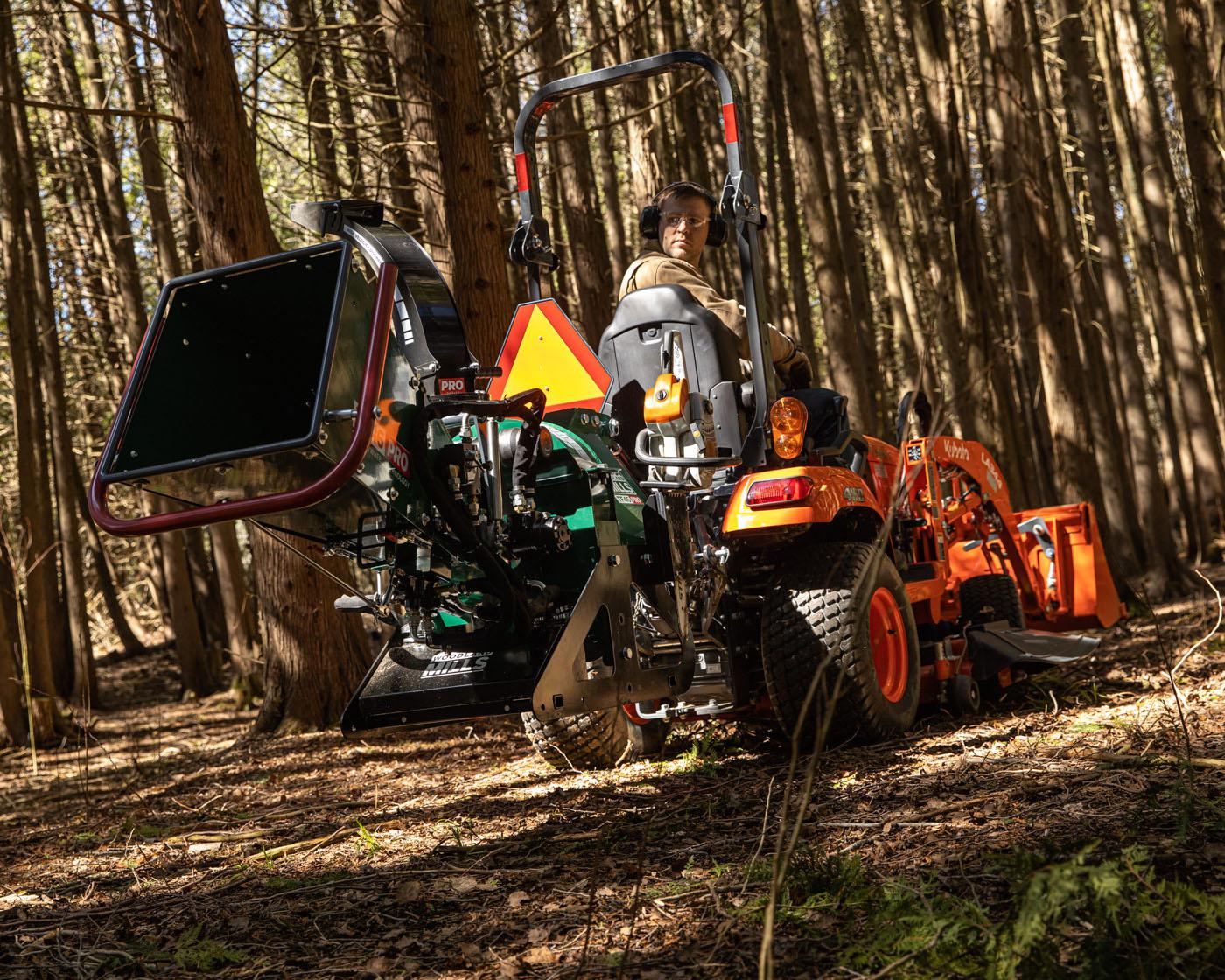 A Woodland Mills TF46 PRO Wood Chipper attached to the back of a tractor on a woodlot.