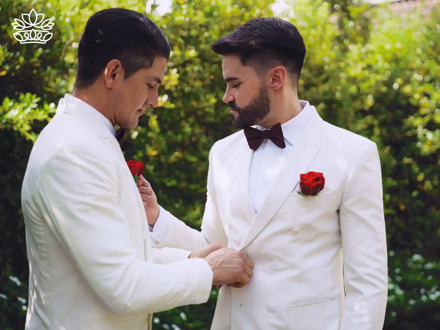 Two men in white suits adjusting each other's jackets, preparing for a wedding. Fabulous Flowers and Gifts - Pride Collection.
