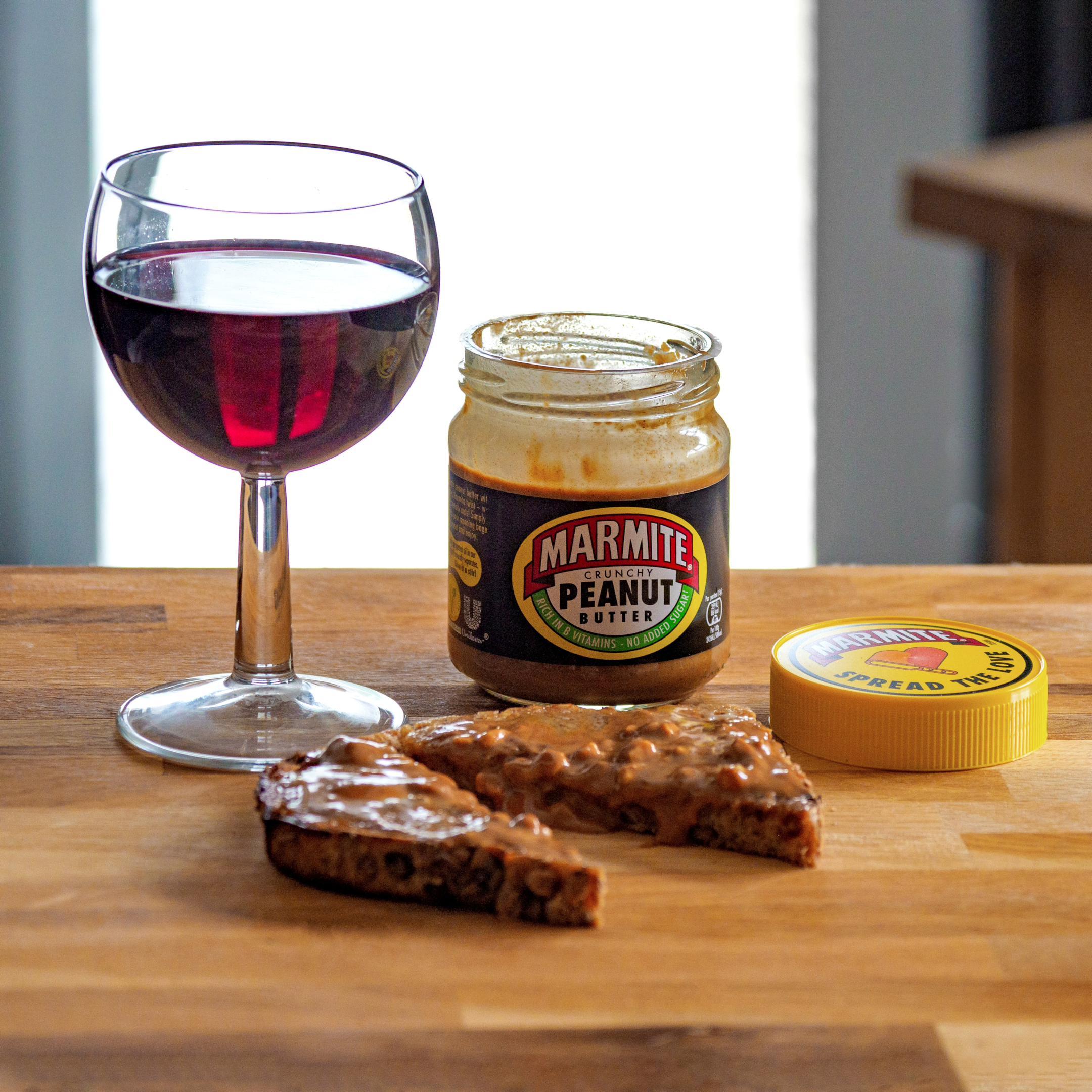 A jar of Marmite peanut butter with an open lid and a slice of bread with peanut butter spread on it.