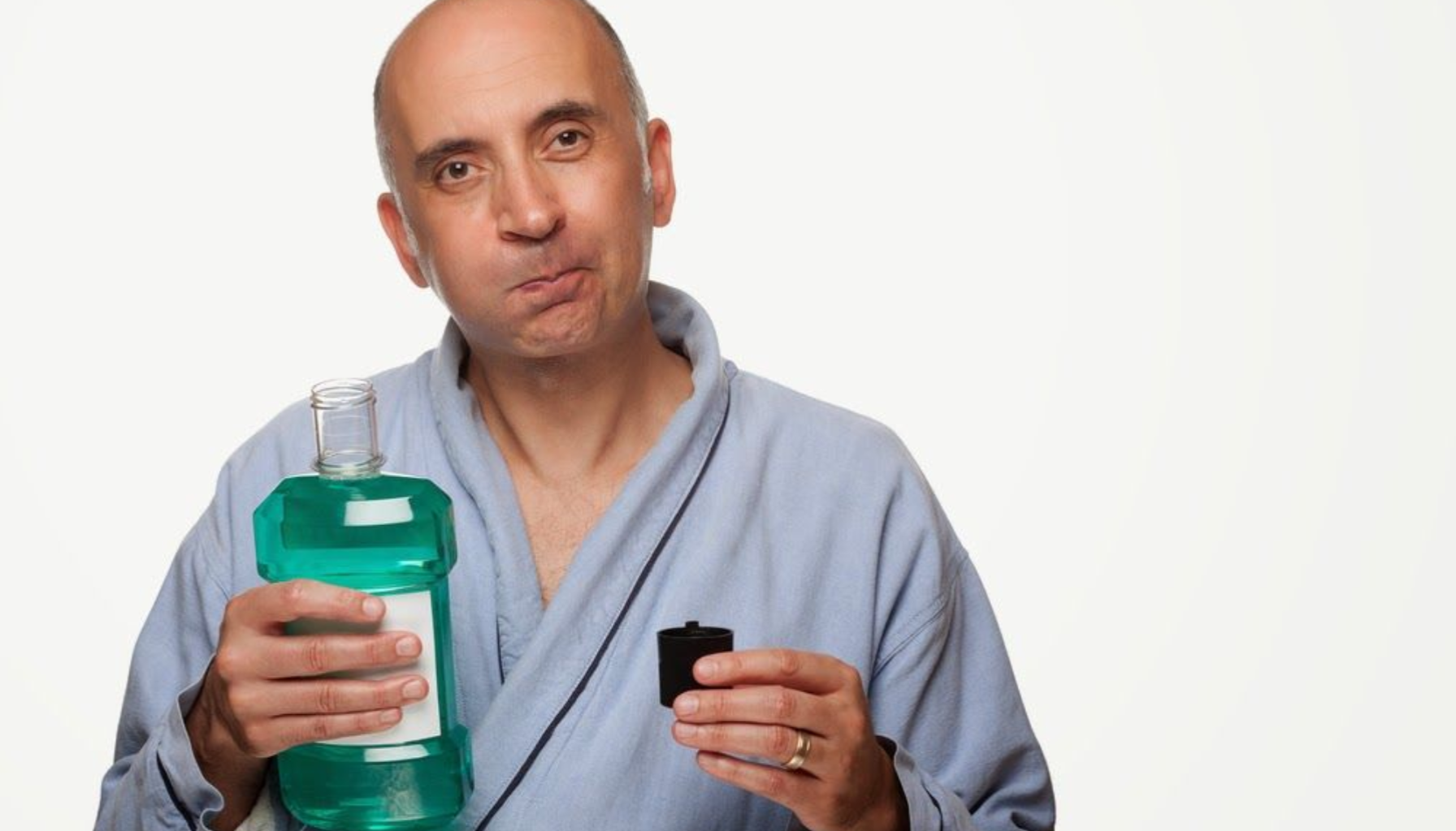 Munnskyll: Når Det Er Nyttig og Når Du Ikke Trenger Det 12 Mann holder munnskyllflaske og målebeger, iført morgenkåpe, med ettertenksomt uttrykk.