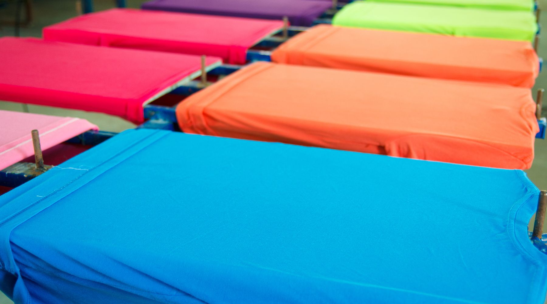 Blue fabric in focus among rows of vibrant orange, pink, and lime fabrics on display.