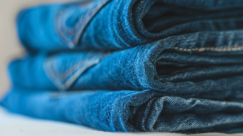 A pile of blue denim jeans placed on top of a white surface.