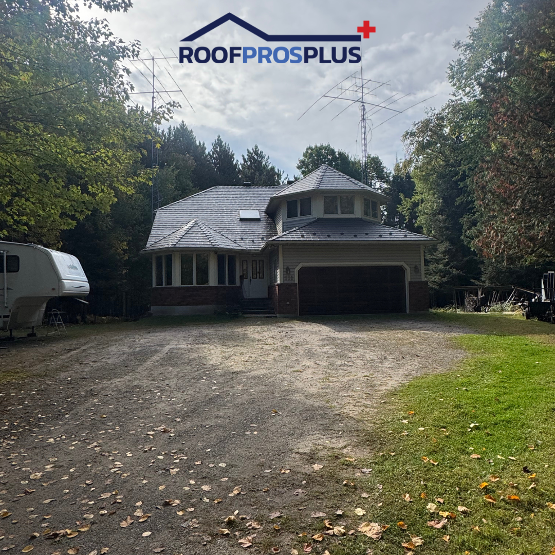 A house with a new metal roof, large driveway and a trailer parked in front, surrounded by greenery and a blue sky.