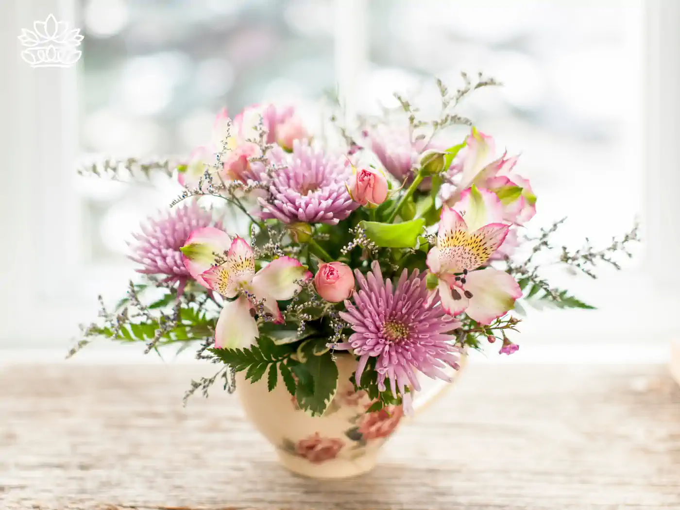 A classic vase filled with an exquisite arrangement of pink asters, alstroemeria, and delicate green foliage, placed by a window with natural light illuminating its beauty. Fabulous Flowers and Gifts: Flower Arrangements Under R500, Delivered with Heart.