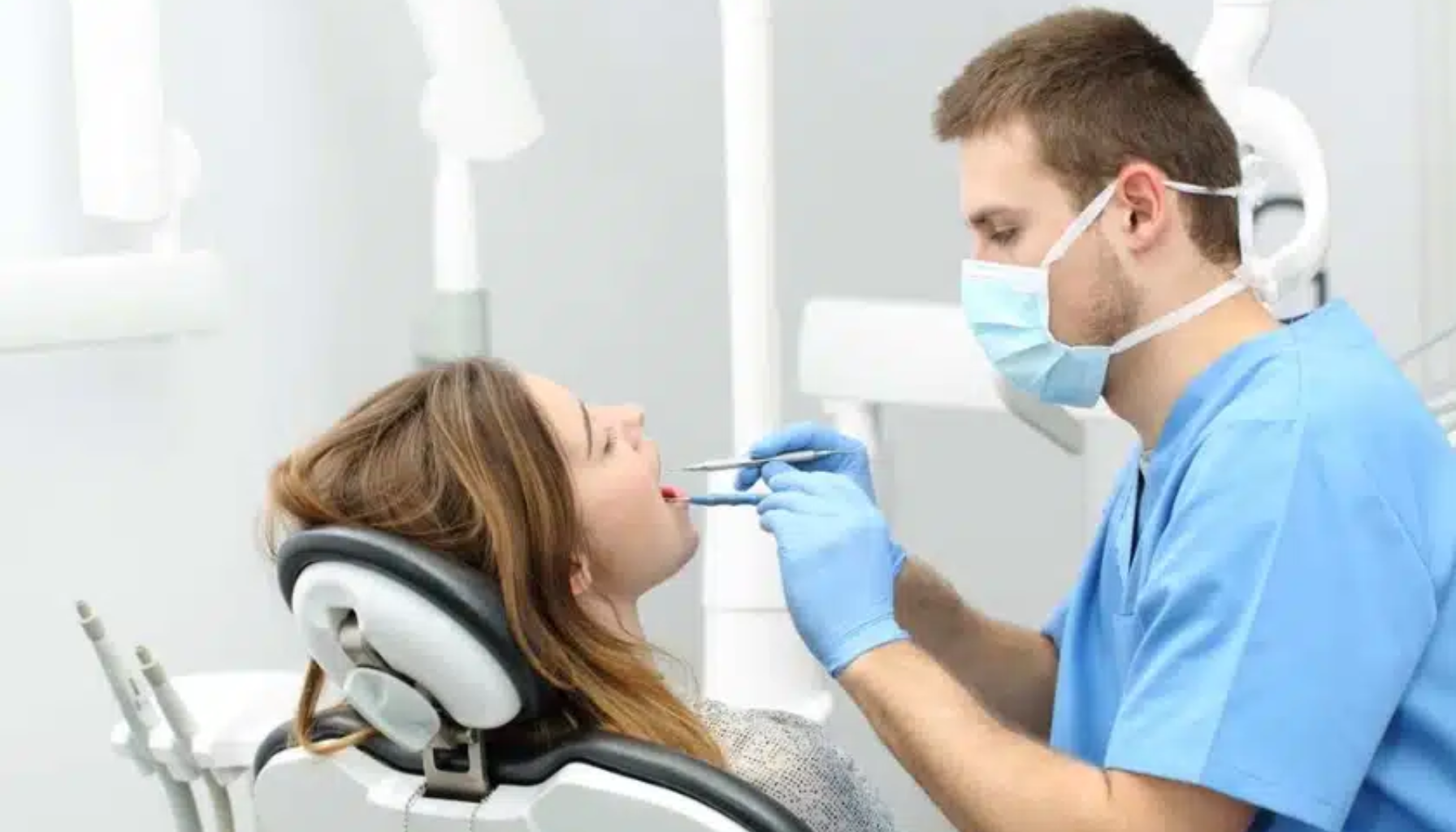 Tannlege med munnbind undersøker en kvinnes tenner i en moderne tannklinikk.