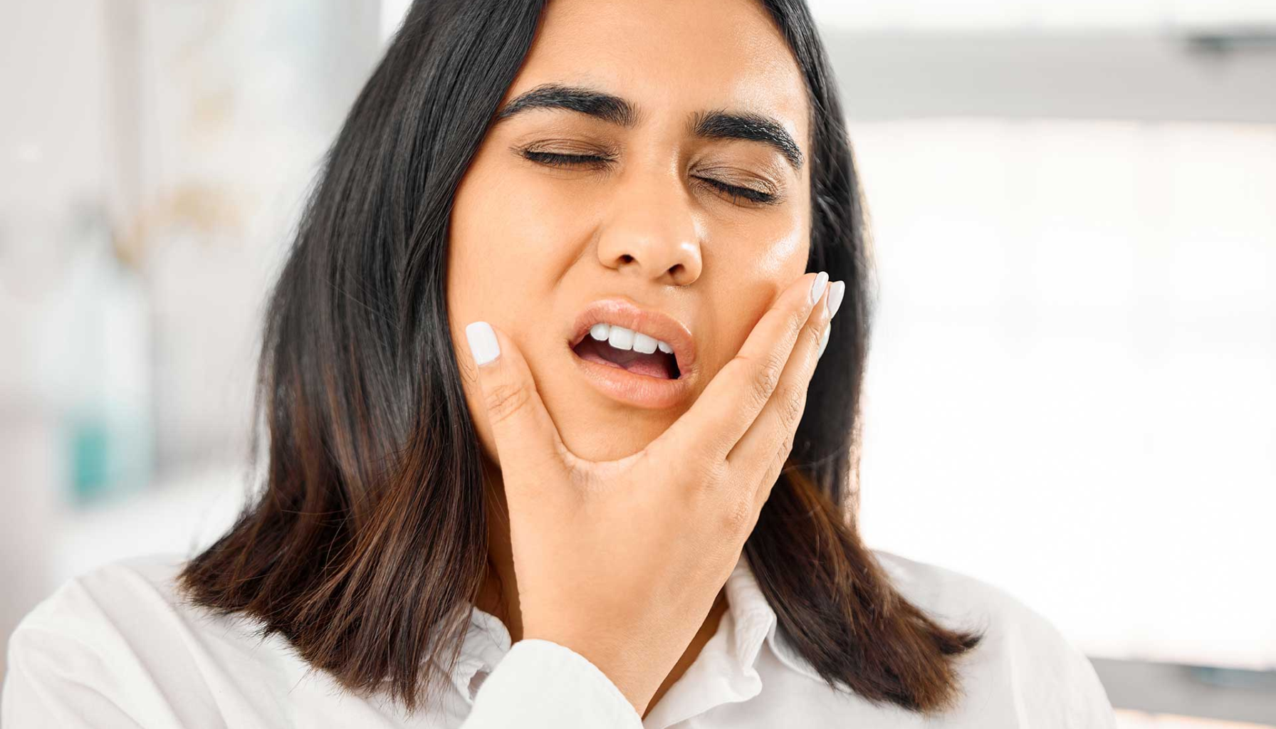 "Kvinne med lukkede øyne holder hånden mot kinnet, ser ut til å ha sterke tann- eller kjevesmerter."