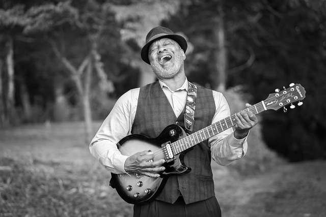 A black and white image of an older man singing while playing a guitar. 