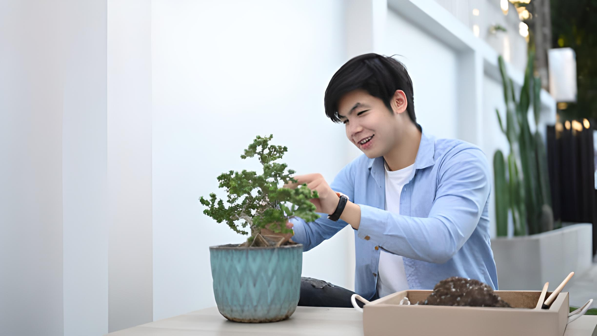 A person smiling while tending to a bonsai tree, reflecting the effects of bonsai care on mental health.