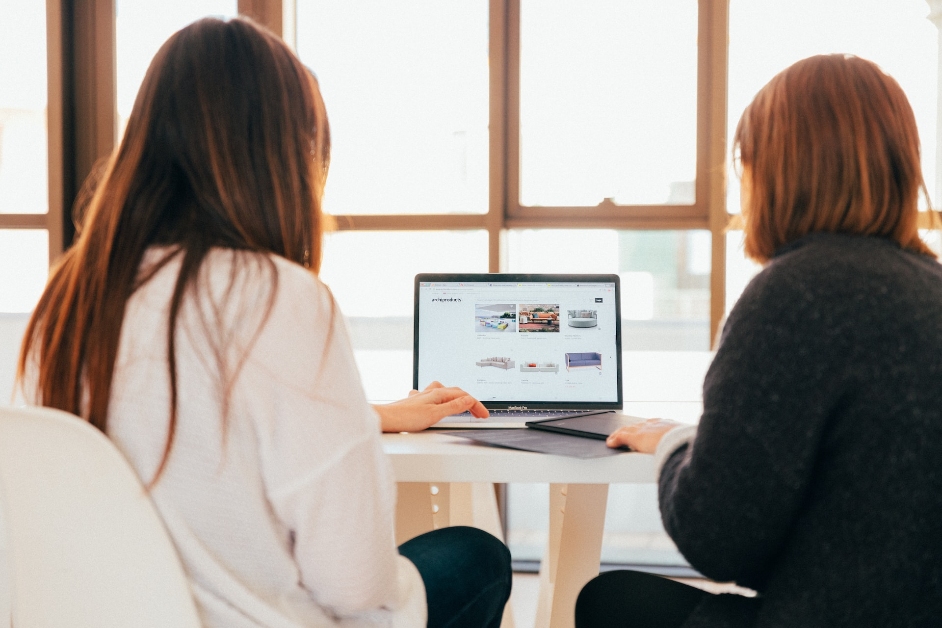 Two woman look at a laptop displaying a furniture eCommerce online store