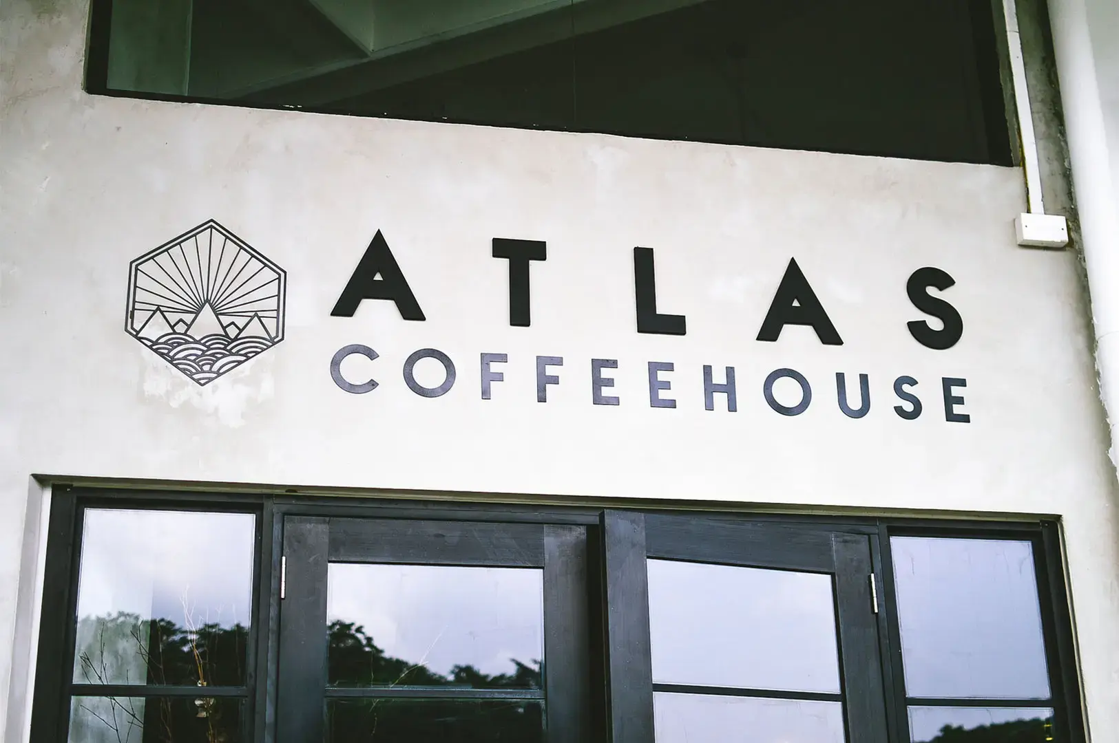 Close-up of the Atlas Coffeehouse sign and logo on a white wall above a window.