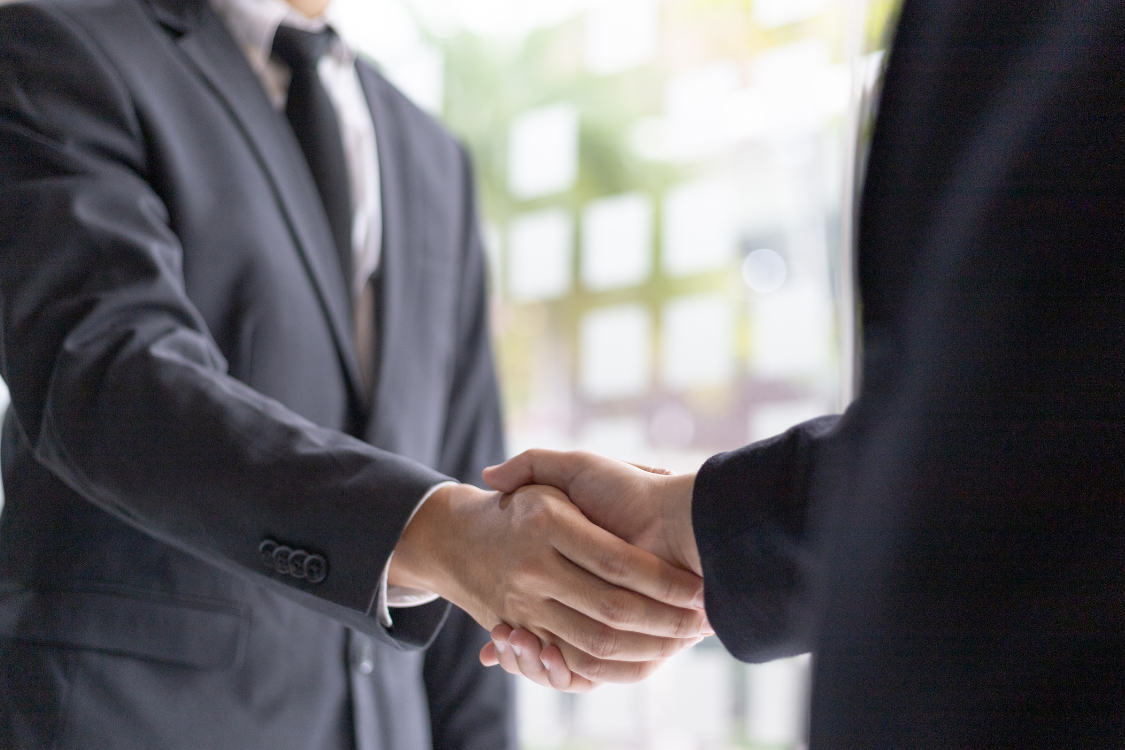 Two professionals in suits shaking hands after reviewing a Confidential Information Memorandum during a business sale.