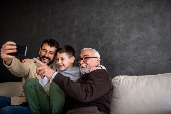 A young dad, his son, and grandpa sitting on the sofa for a selfie.