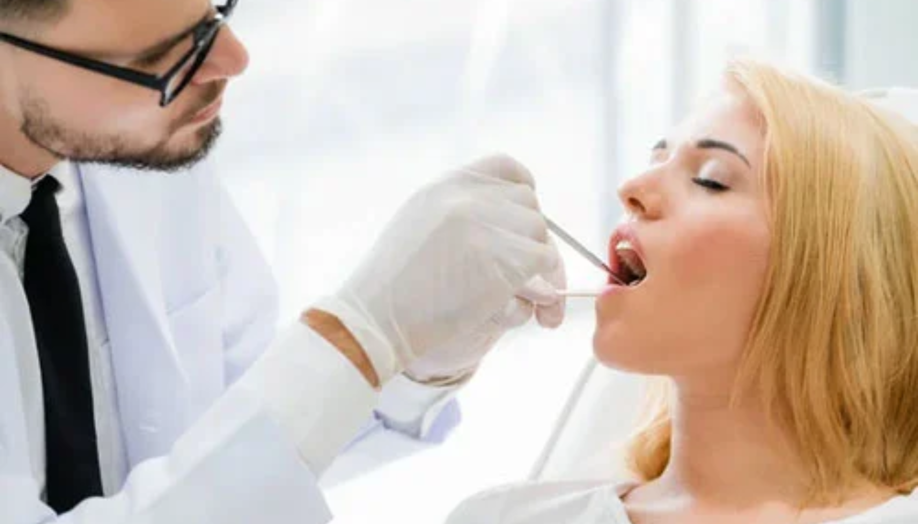 Tannlege undersøker pasientens tenner med speil og hansker mens kvinnen sitter avslappet i tannlegestolen.