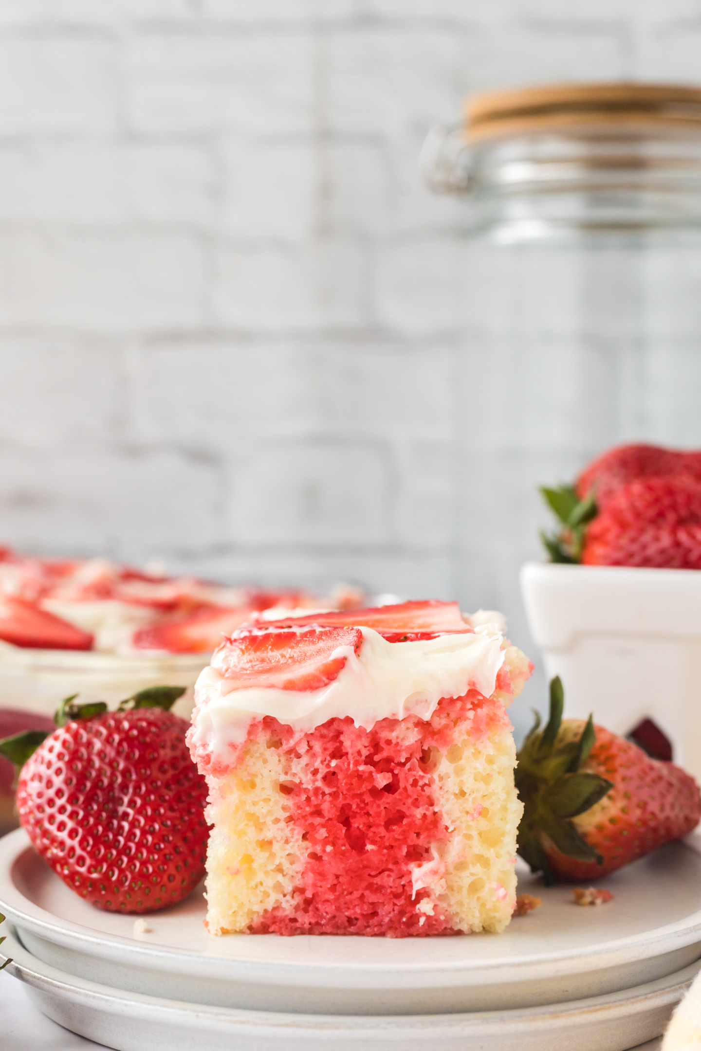 slice of strawberry poke cake on a plate with fresh strawberries