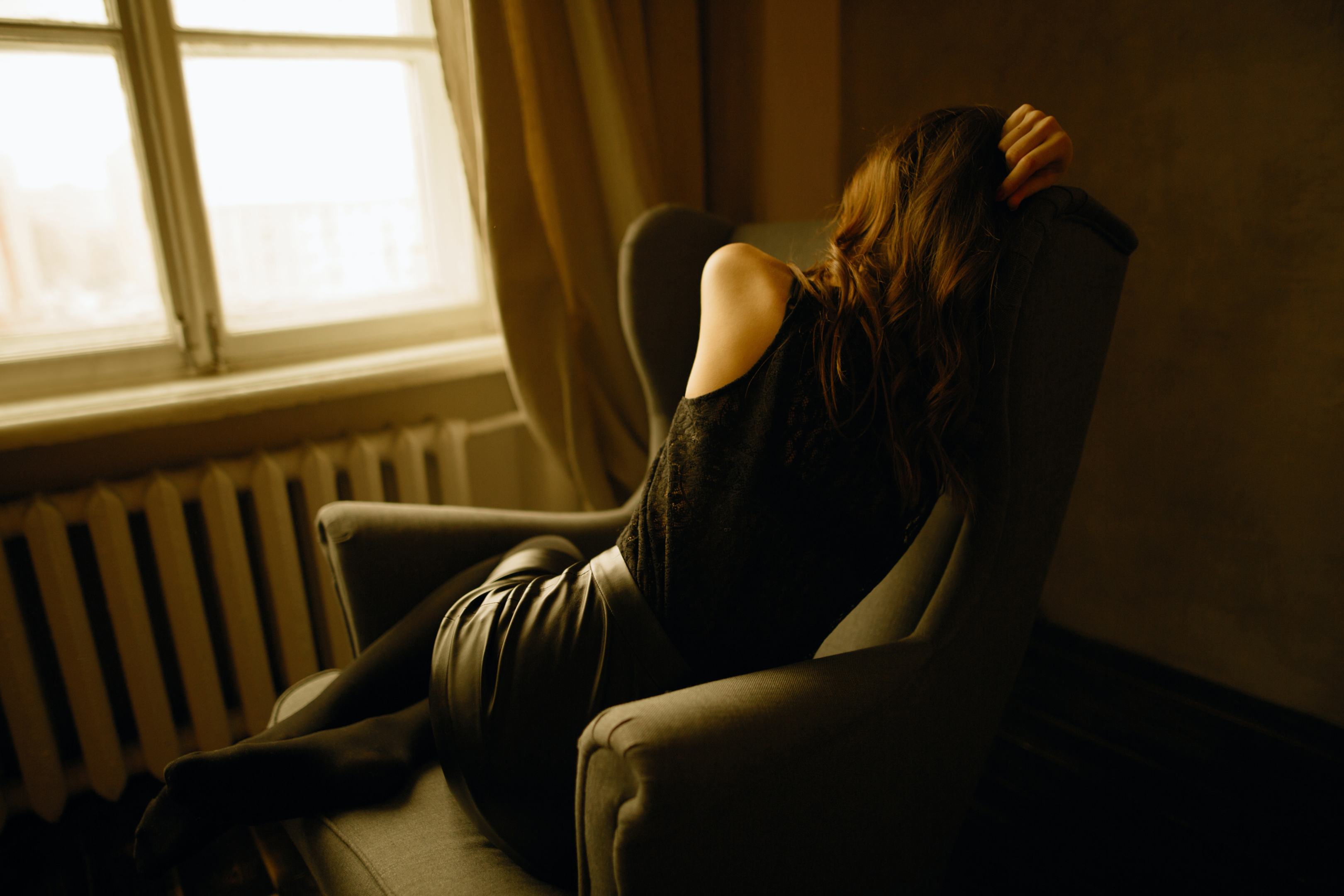 Depressed woman sitting in a chair by a window in the dark