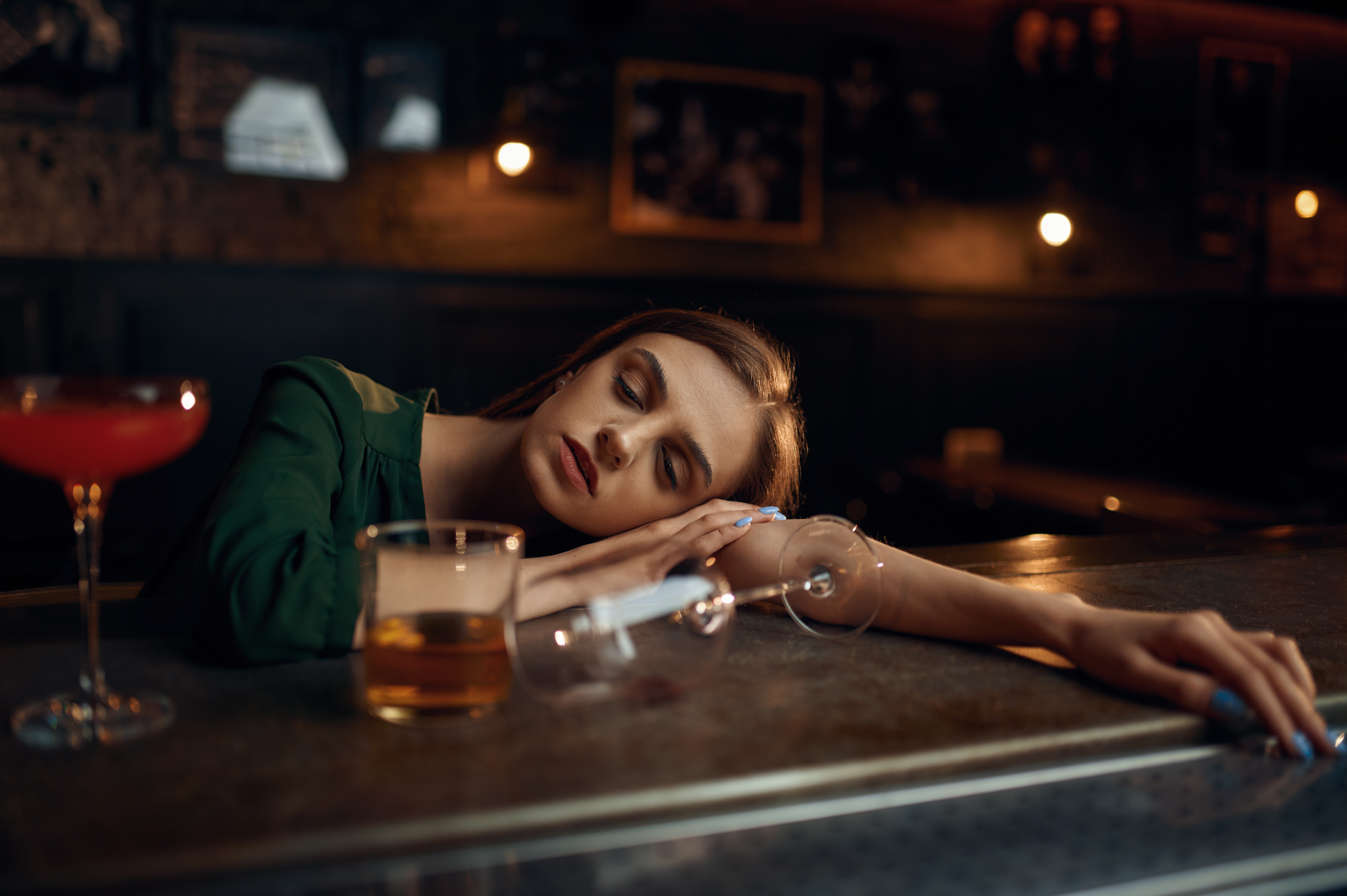 Woman slumbering at a bar table, surrounded by empty glasses.