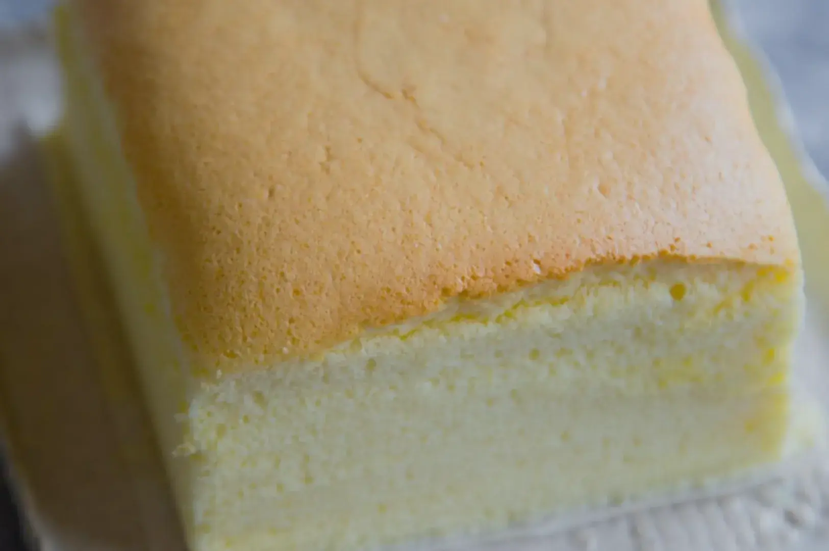 A close-up of a fluffy yellow cake with a smooth top and a light golden-brown crust.