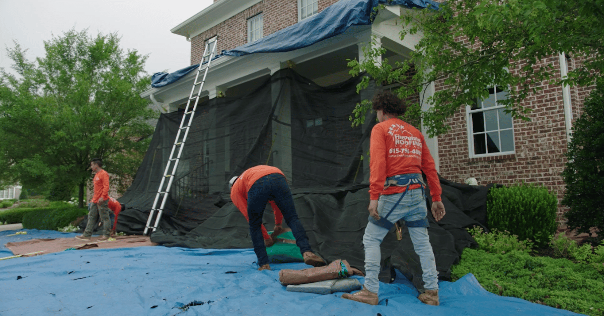 Roofing team in protective gear securing edge tarps and prepping tools as they complete the front-side protection of a residential property in Nashville, TN.