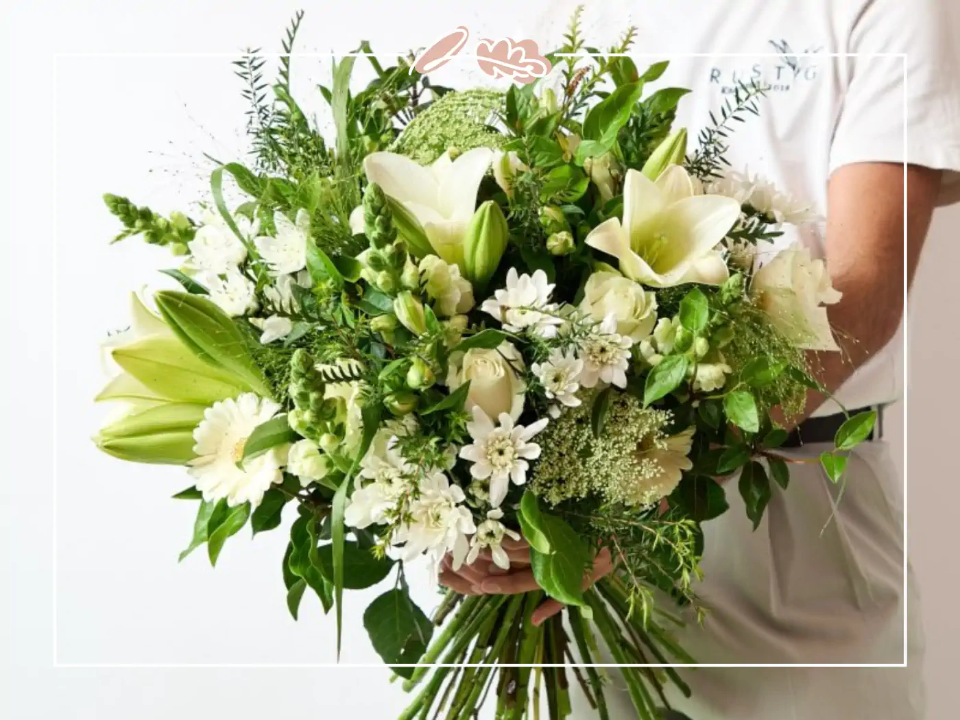 A beautiful bouquet of white lilies, roses, and various white flowers with green accents, carefully held by a person in a white shirt. Fabulous Flowers and Gifts.