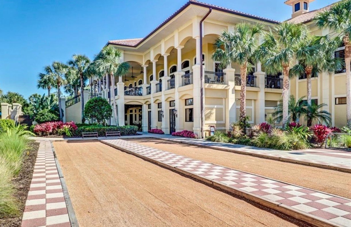The image depicts a Mediterranean-style clubhouse with elegant architecture, surrounded by beautifully landscaped gardens, creating a welcoming focal point for the gated community in Estero, FL. The clubhouse serves as a hub for social events and activities, enhancing the lifestyle of residents near the Grandezza Golf Course and other amenities.
