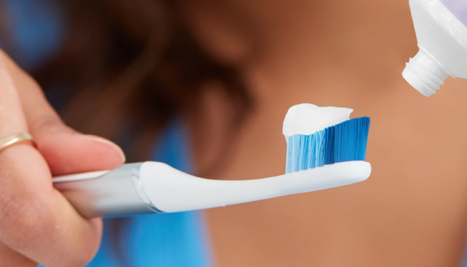 Person klemmer tannkrem på en hvit tannbørste med blå børstehår.