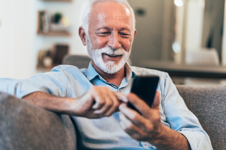 Older man with gray hair sitting on a sofa sending a text. 
