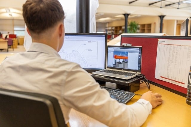 Man working looking at both laptop and computer screen
