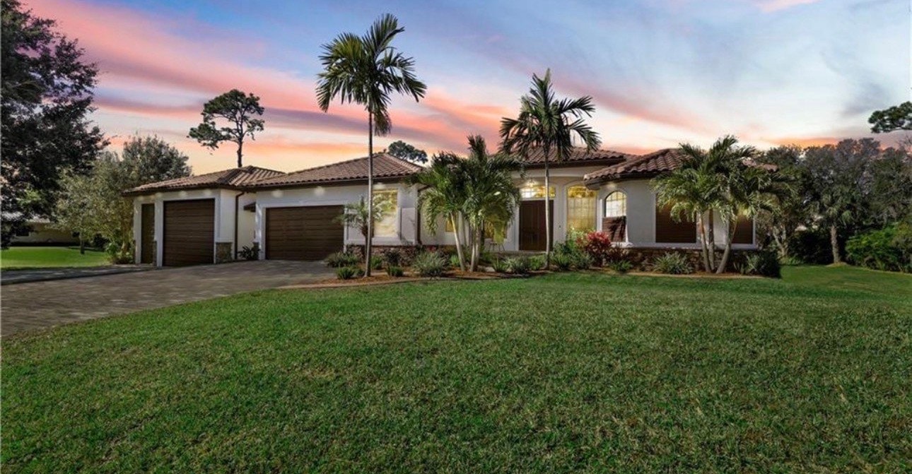 The image depicts a spacious 5000 square foot home nestled on a 2-acre lot in Florida, surrounded by lush palm trees, showcasing an expansive outdoor living space. This property is part of the desirable Livingston Woods community in Naples, offering a private and serene environment.