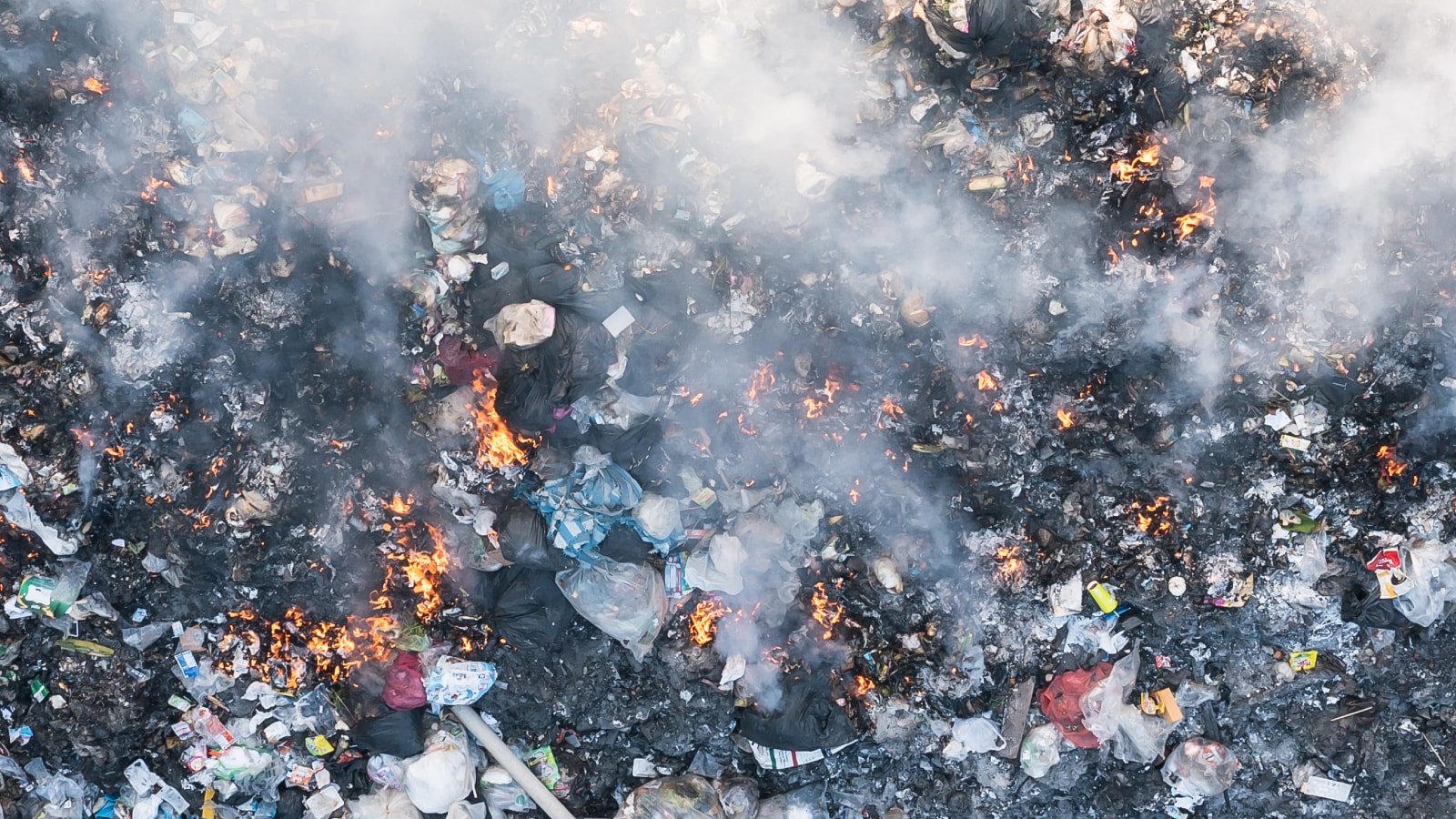 Foto udara dari pembakaran sampah besar-besaran yang menghasilkan asap dan api di area terbuka.