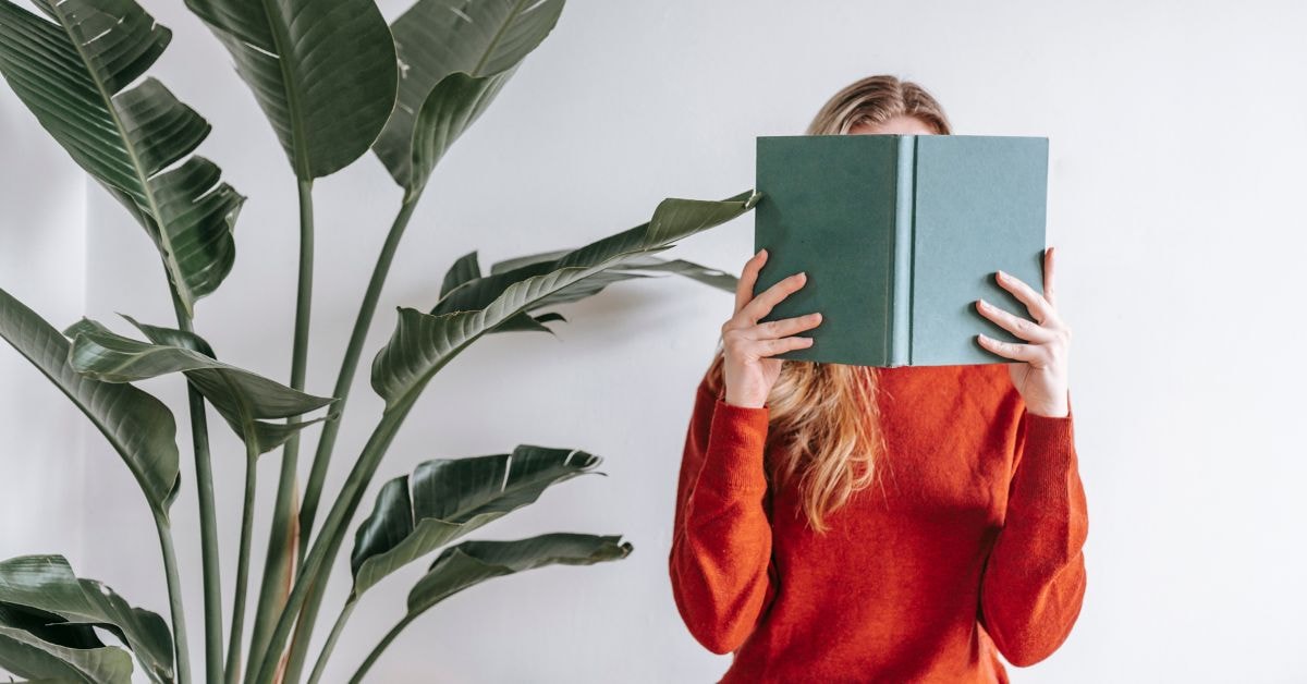 Woman learning how to file state taxes only, reading a book with a leafy plant in the background.