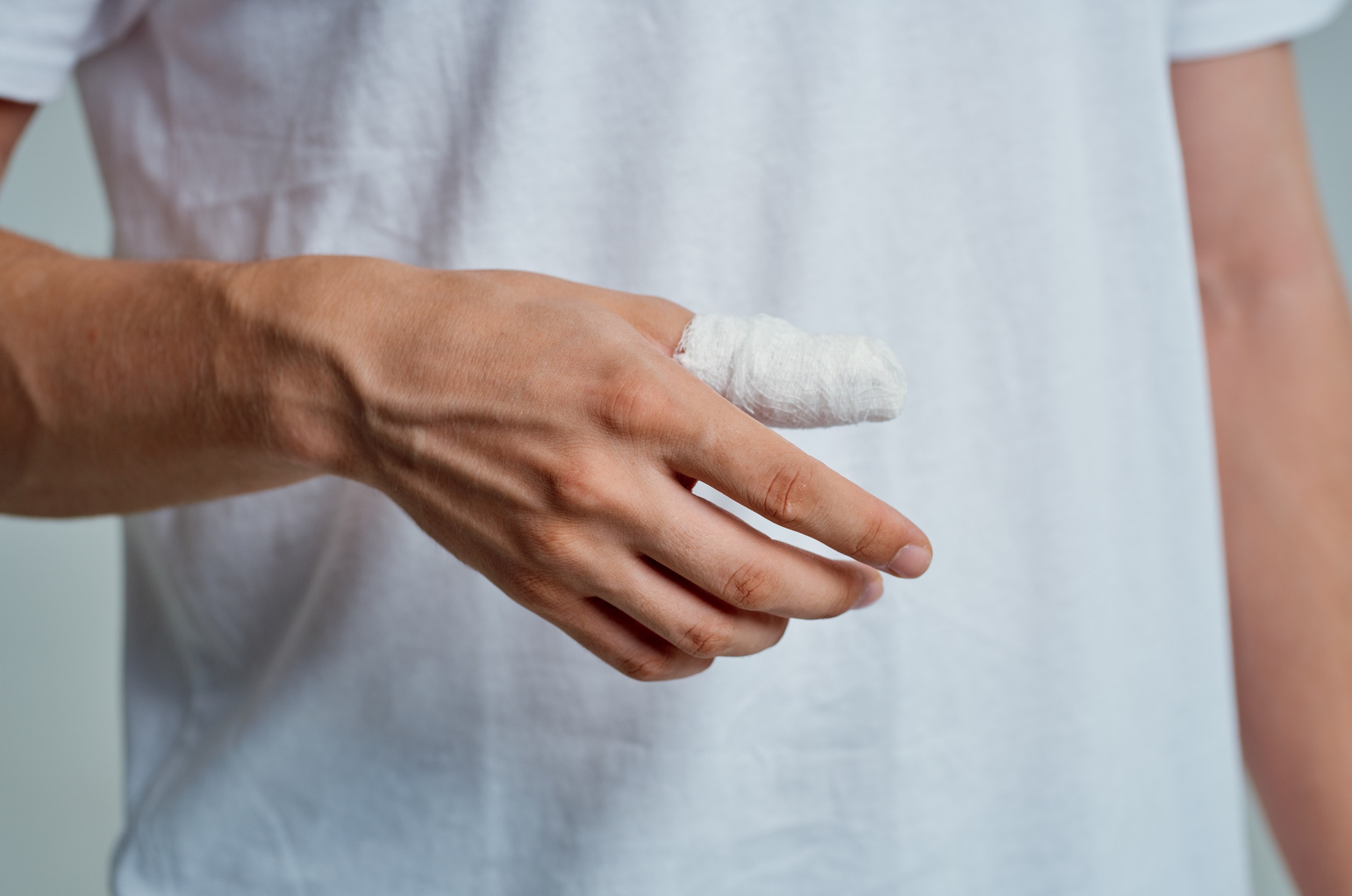 A man in a white t-shirt with a bandage on his thumb injuries suffers permanent or recurring pain