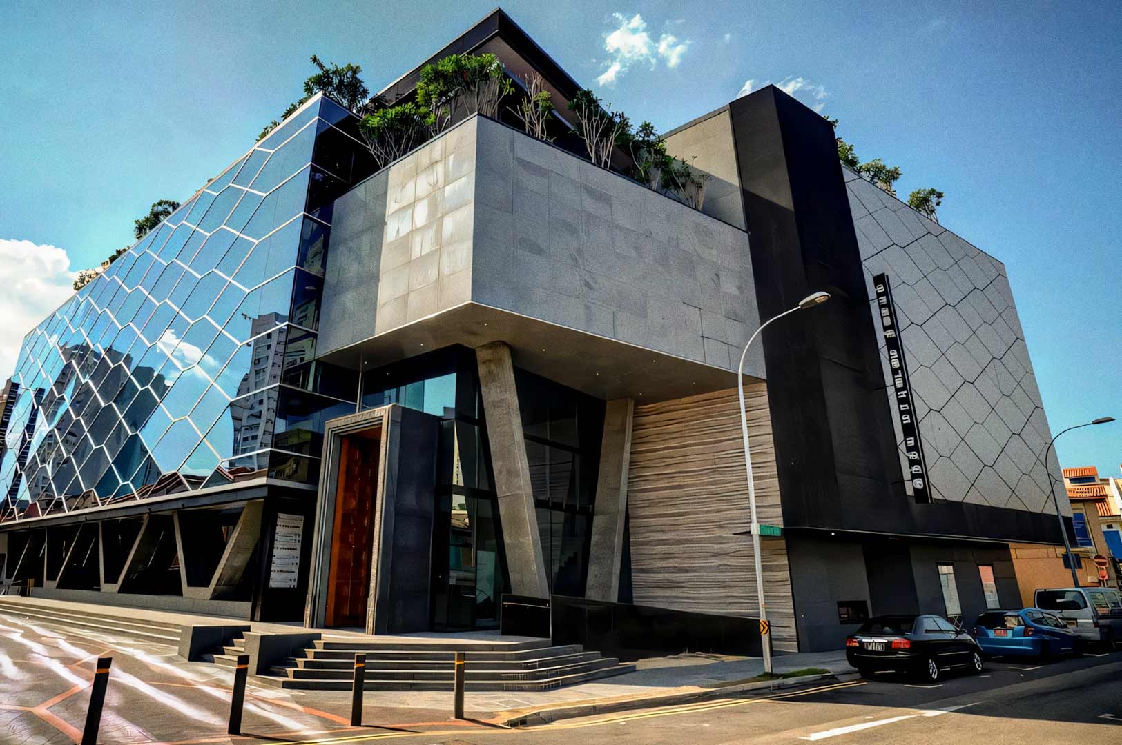 The modern glass-and-concrete façade of the Indian Heritage Centre, featuring angular architectural lines and reflective patterned windows along a quiet street.