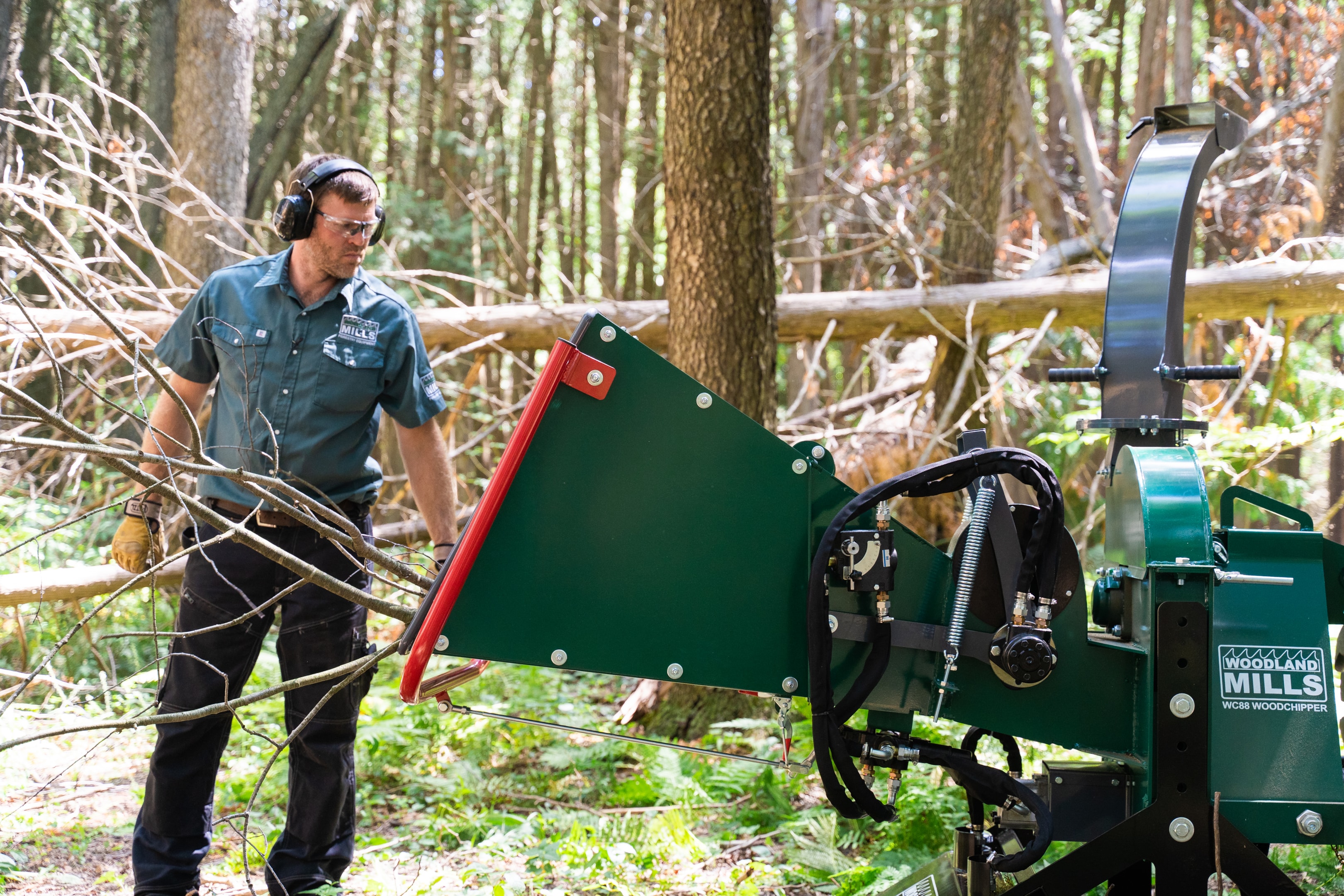 A man feeds tree branches into his Woodland Mills Wood Chipper in a forest.