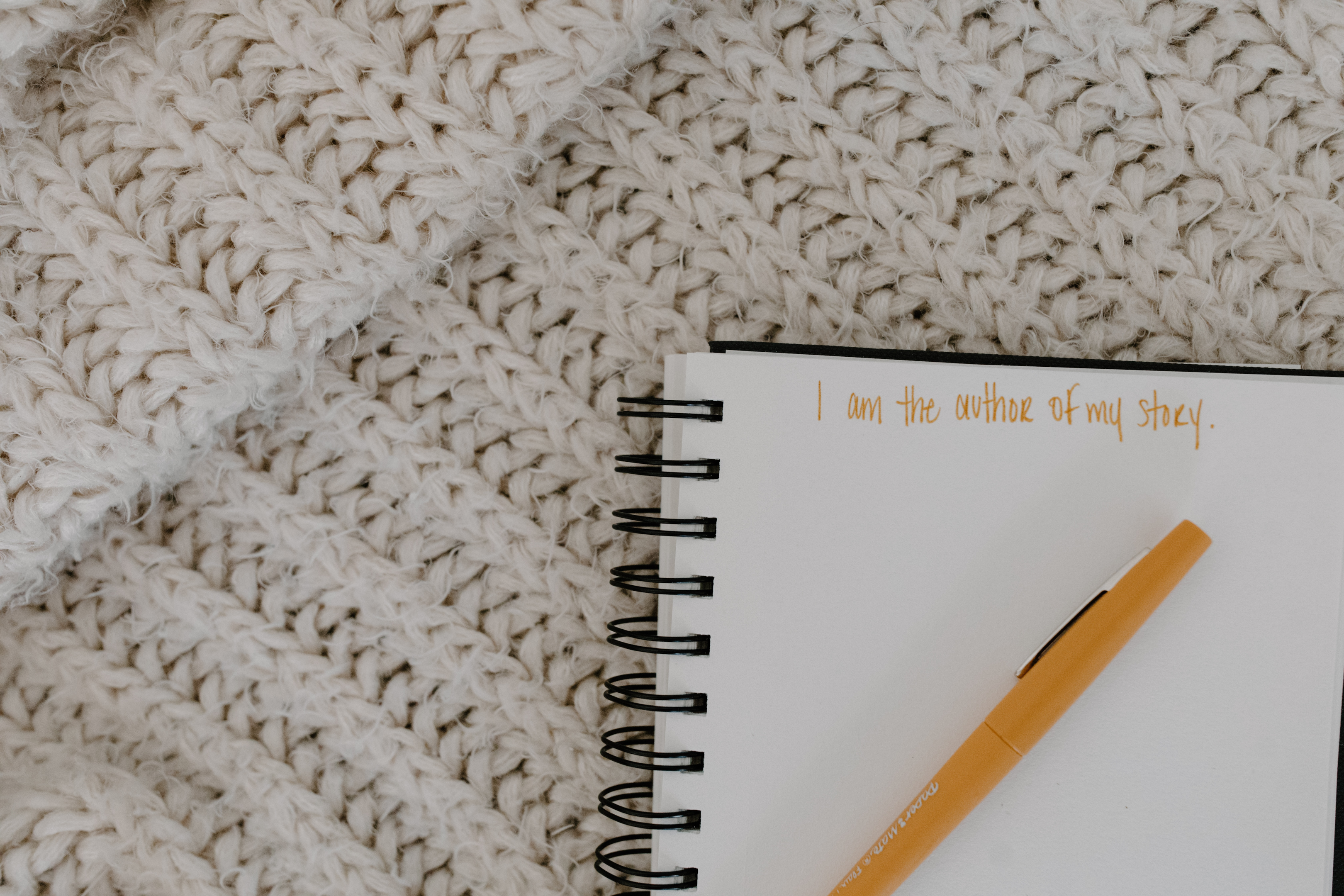 A spiral notebook and pencil on a cozy blanket with "I am the author of my story" written on it