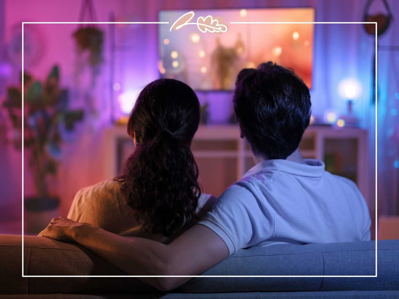 A couple watching TV in a dimly lit room with purple and blue lighting, creating a relaxing movie atmosphere - Fabulous Flowers and Gifts.