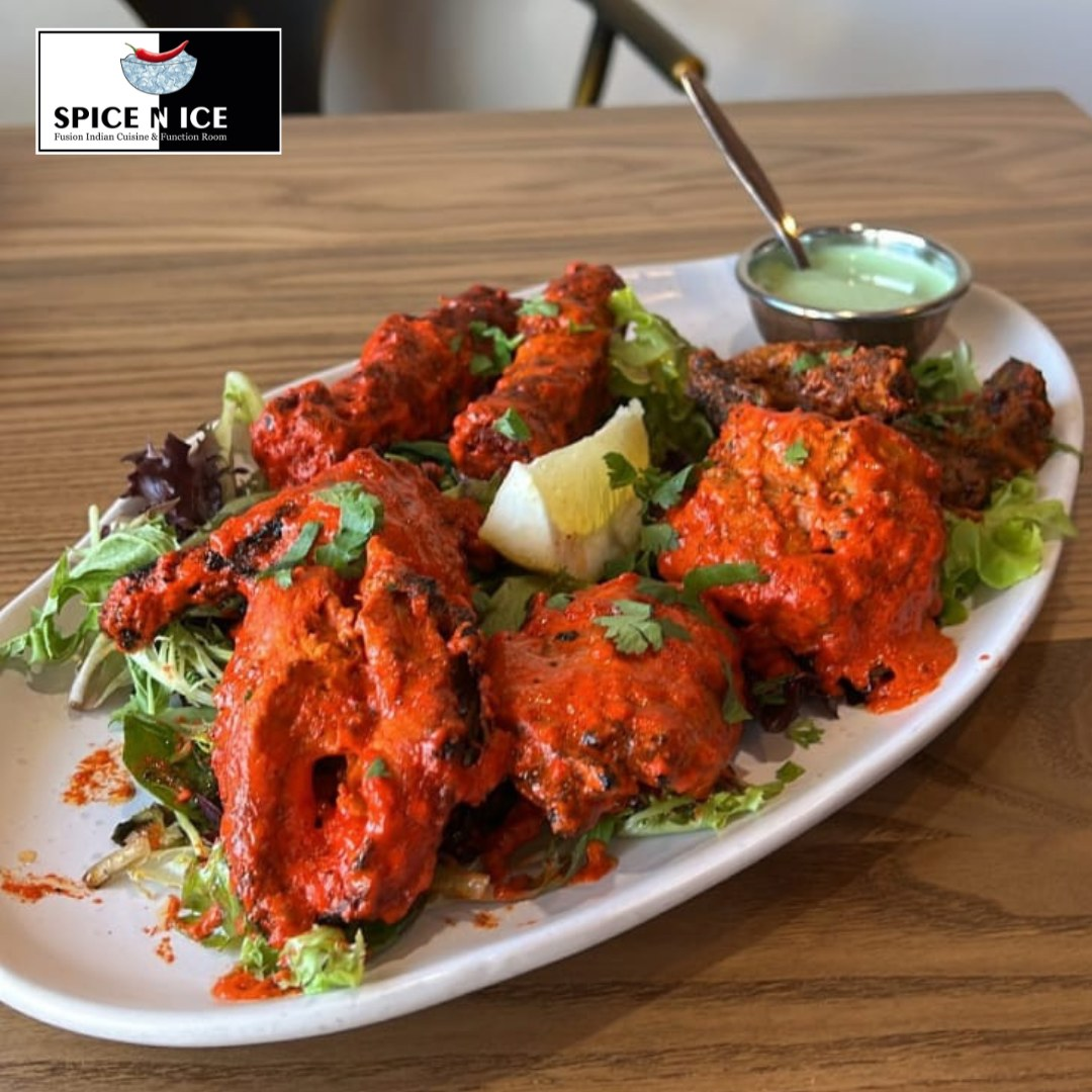 Golden brown chicken tikka on a skewer, served with vibrant green cilantro chutney on a white plate.
