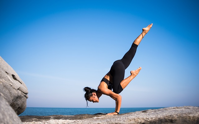 An image of a woman doing a yoga handstand pose on a cliff. 