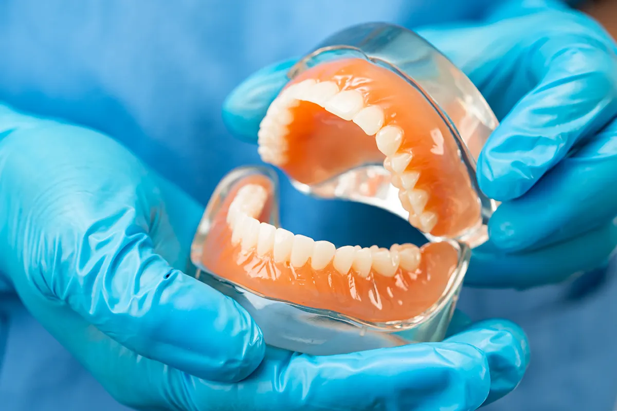 Dental professional holding complete denture prosthesis with blue gloves