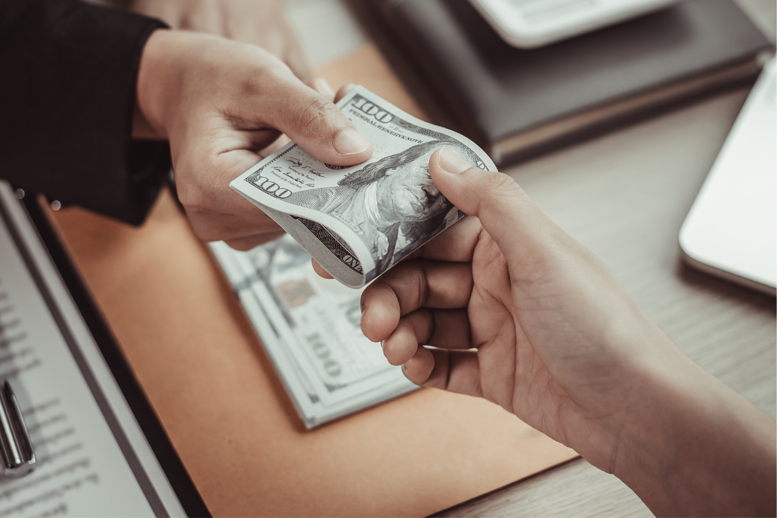 Close-up of hands exchanging U.S. dollar bills representing salary or contractor payment