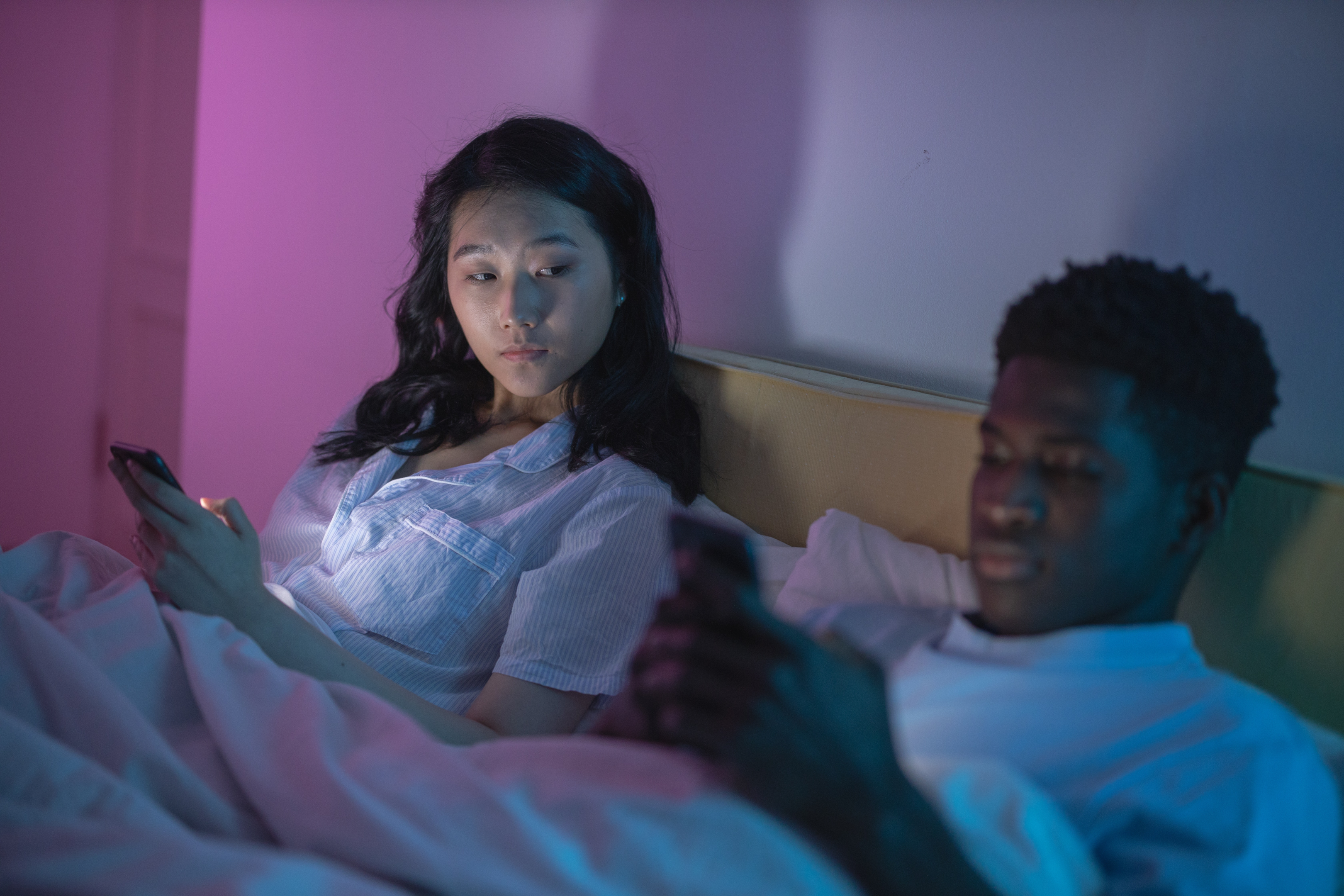 couple in bed, women looking over boyfriend shoulder with jealousy 