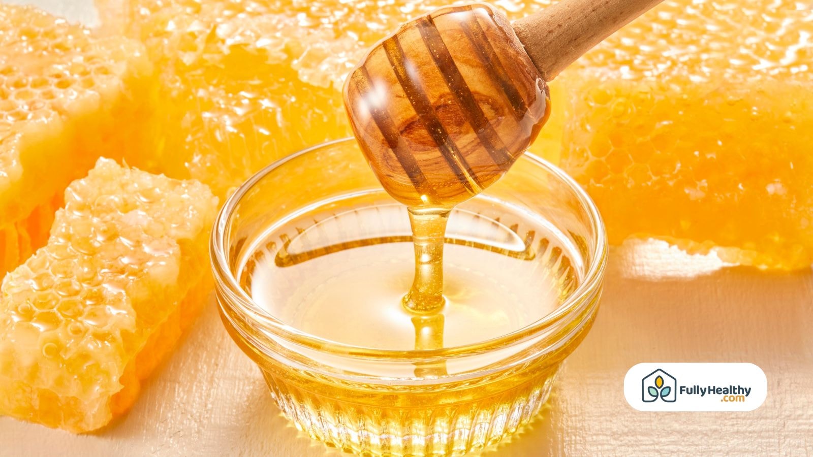 Golden honey dripping from dipper into glass bowl with fresh honeycomb behind
